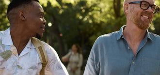 Two younger men smiling and walking outdoors in a park on a sunny day—representing open conversations and support around prostate cancer awareness.
