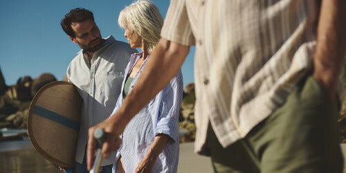 Adults walking together on a sunny beach, casually talking and enjoying the day, featured in an article about urge urinary incontinence and bladder spasms.