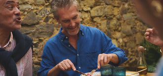 Group of men socialising at an outdoor meal, smiling and chatting, featured in an article about different types of male incontinence.