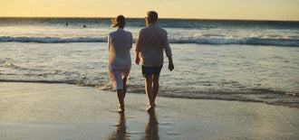Older couple walking hand-in-hand along the shoreline at sunset, representing emotional and physical connection during menopause.