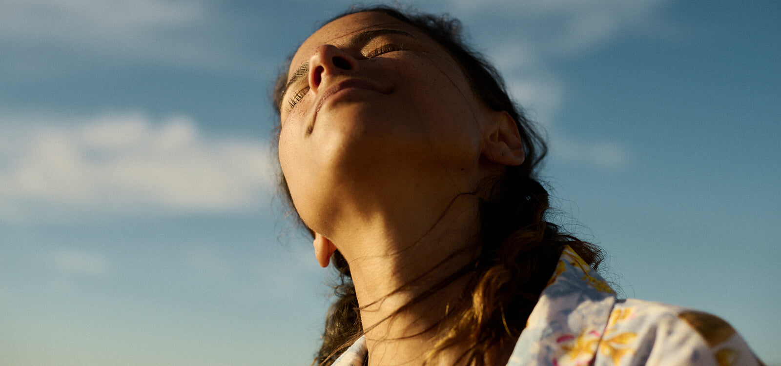 Close-up of a woman basking in sunlight with her eyes closed, symbolising confidence and wellbeing in an article about losing menopause belly fat.
