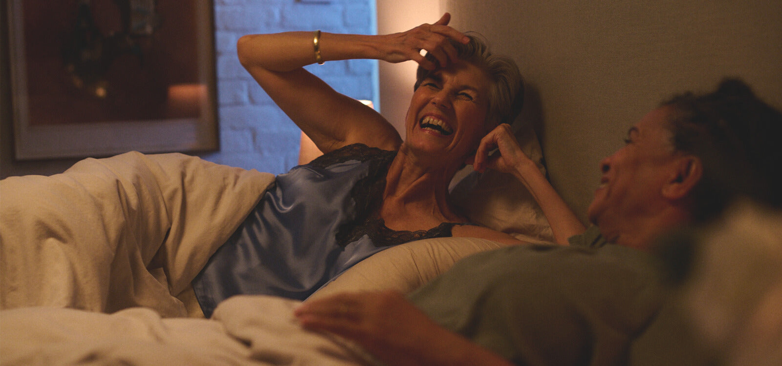 Two older adults sharing a joyful moment in bed at night, illustrating comfort and connection in an article about adult bedwetting and nocturia.