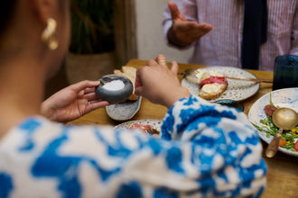 Close-up of a woman’s hands seasoning food at a colourful table spread, used in an article about menopause-friendly foods that support weight loss