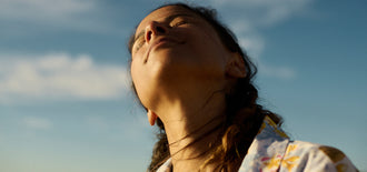 Close-up of a woman basking in sunlight with her eyes closed, symbolising confidence and wellbeing in an article about losing menopause belly fat.