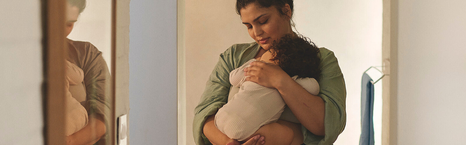 Pregnant woman holding her baby in a soft-lit bathroom, reflecting on health and changes during pregnancy