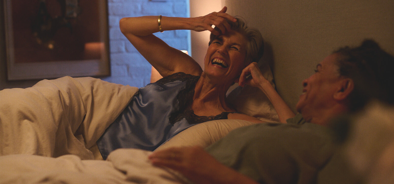 Two women laughing while lying in bed