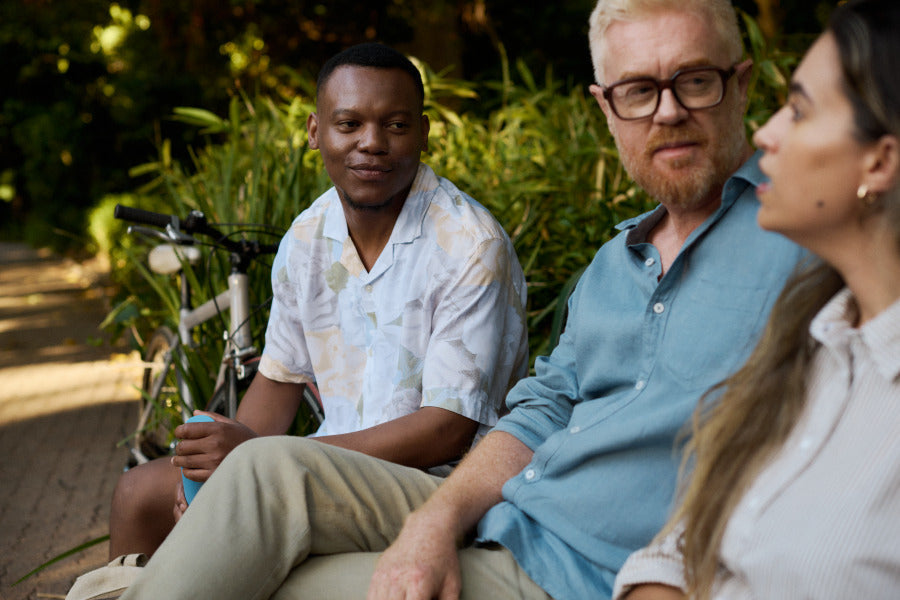 Three adults sitting on a bench outdoors, having a thoughtful conversation next to a bicycle, featured in an article about anxiety-related incontinence and how to manage it