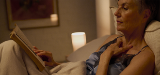 Older woman in nightwear reading a book in bed, softly lit by a bedside lamp, illustrating a calm moment in an article about understanding light bladder leakage and its management.