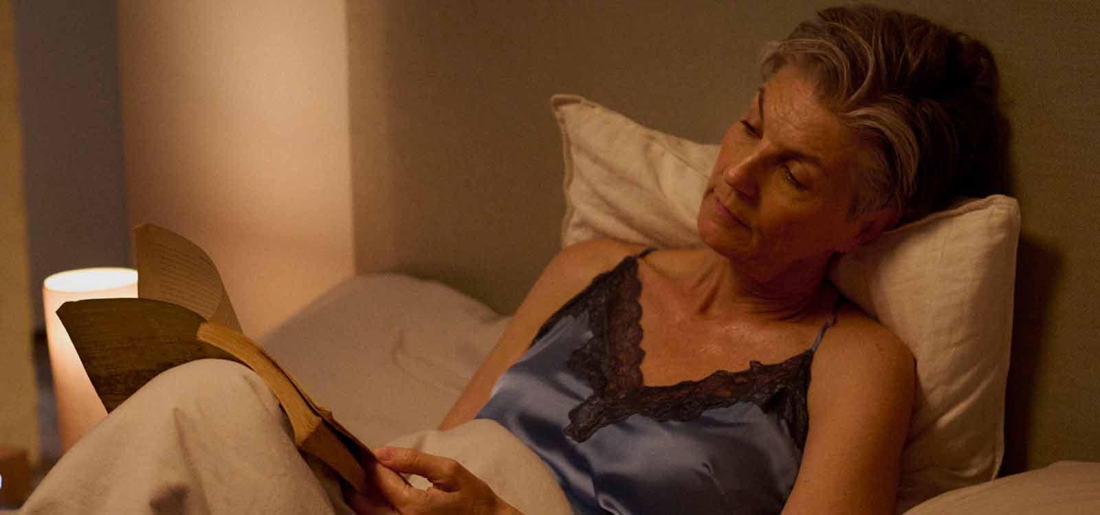 Older woman relaxing in bed, reading a book under warm lighting, illustrating the overlooked side effects of menopause.