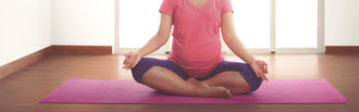 A pregnant woman sits on a yoga mat