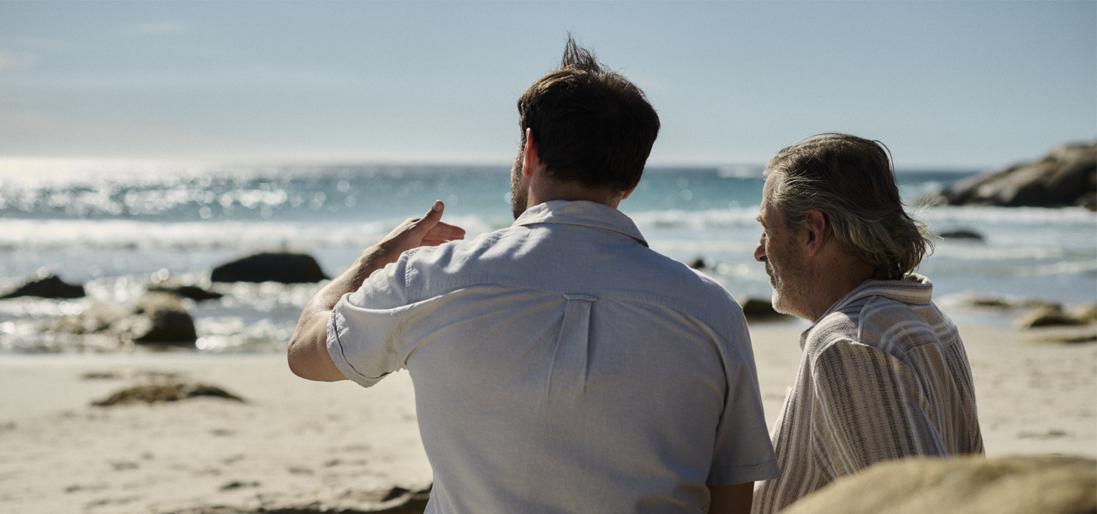 two men sit on a beach talking