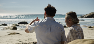 two men sit on a beach talking